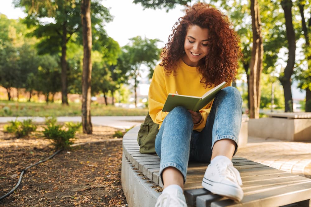 A teenage girl outside reading about adolescent mental health treatment in NJ