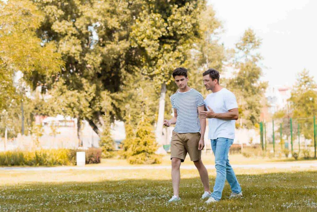 Father and teenage son walking together outdoors while having a supportive conversation.
